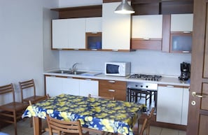 A compact kitchen with a microwave, stove, sink, and a dining table with chairs.