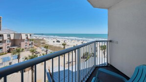 A balcony with a view of a beach and ocean, a building with multiple floors, and a clear blue sky. - Ocean Annie's Oceanview Studio,Scenic Views,Pools! (Myrtle Beach)