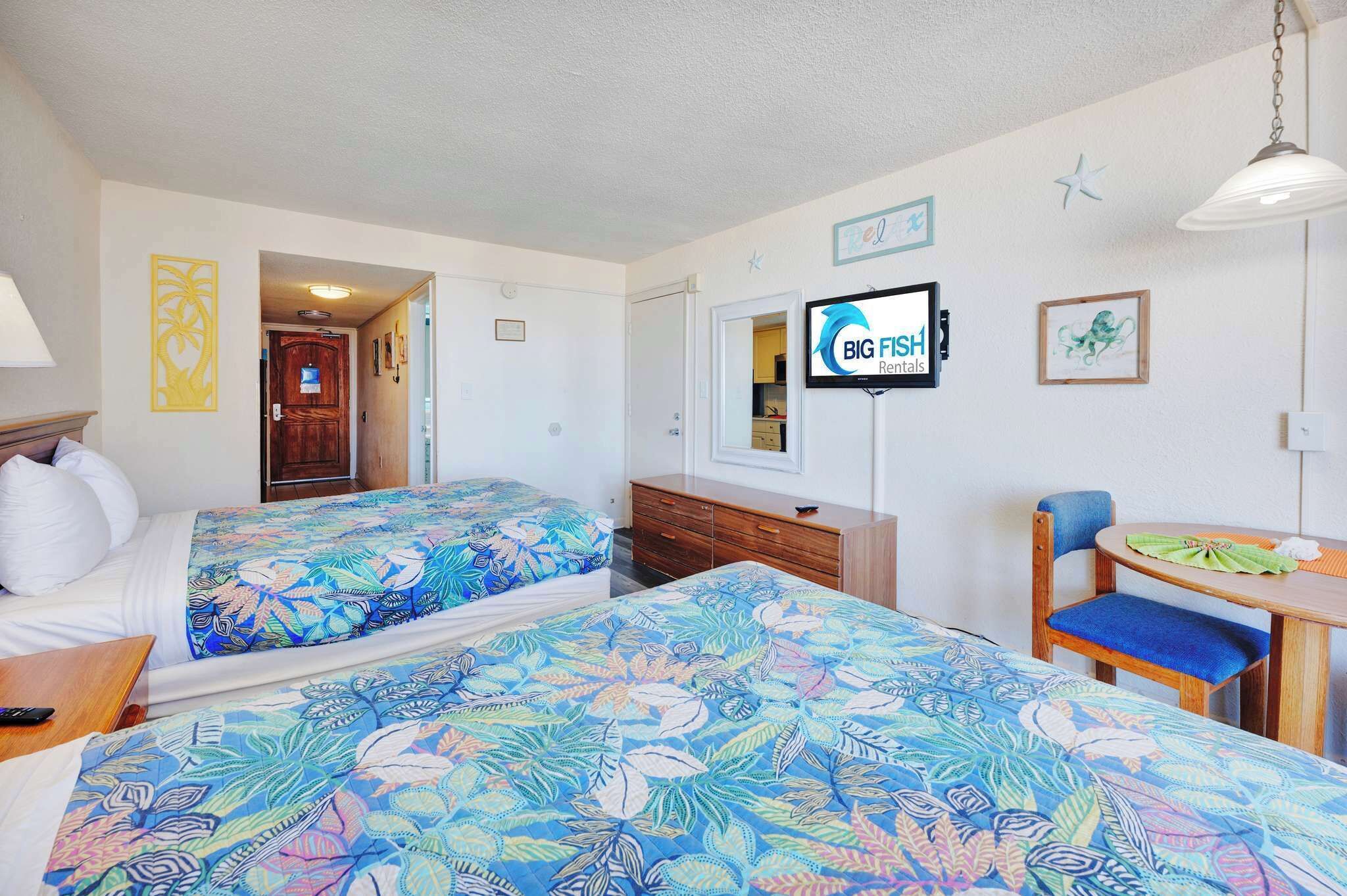 A hotel room with two beds, a TV, a desk with a chair, and a wooden dresser.