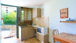 A compact kitchen with a built-in oven, a dining table with a patterned tablecloth, and a view of greenery outside. - Agapi Studio in Kalami (Corfu)