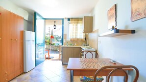 A compact kitchen with a dining area, a refrigerator, a sink, and a window overlooking a scenic view. - Agapi Studio in Kalami (Corfu)