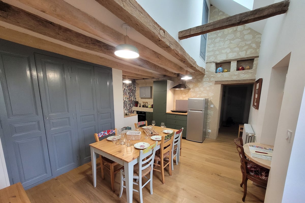 A cozy kitchen with wooden beams, a dining table set for four, and a refrigerator.