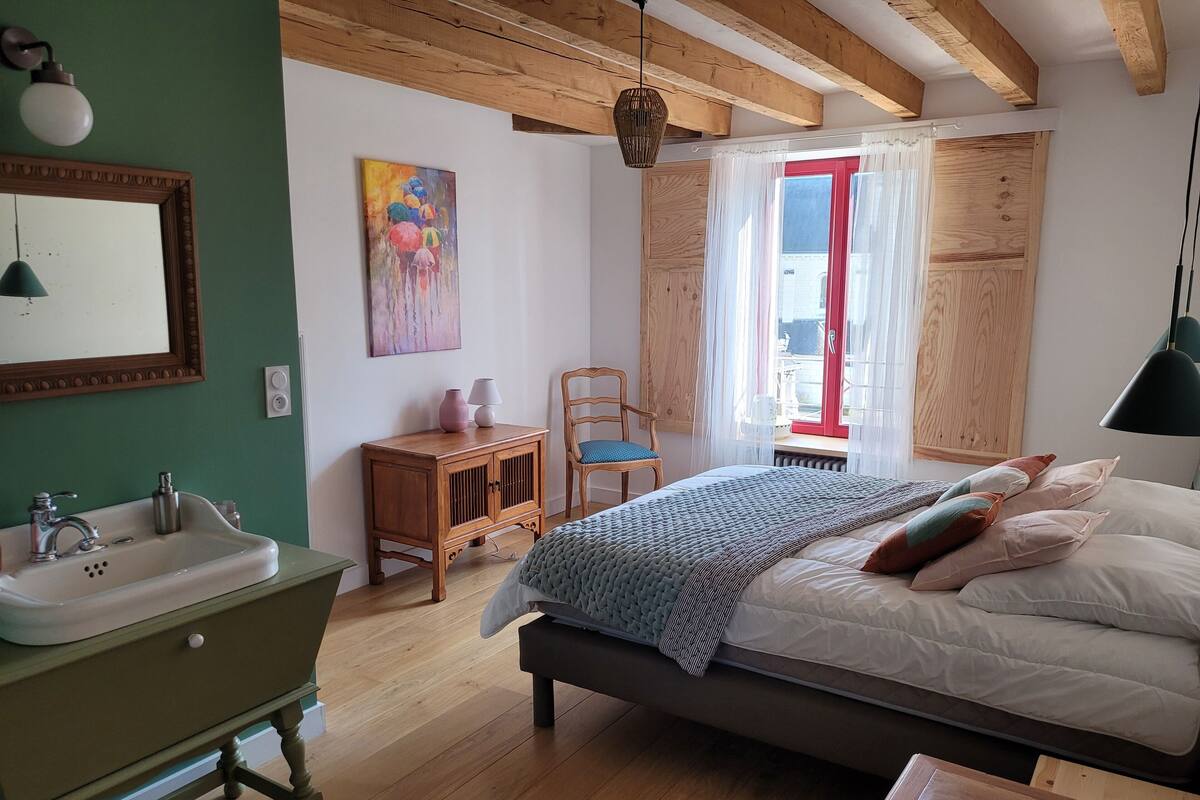 A bedroom with a bed, a wooden cabinet, a chair, a window with curtains, and a painting on the wall.