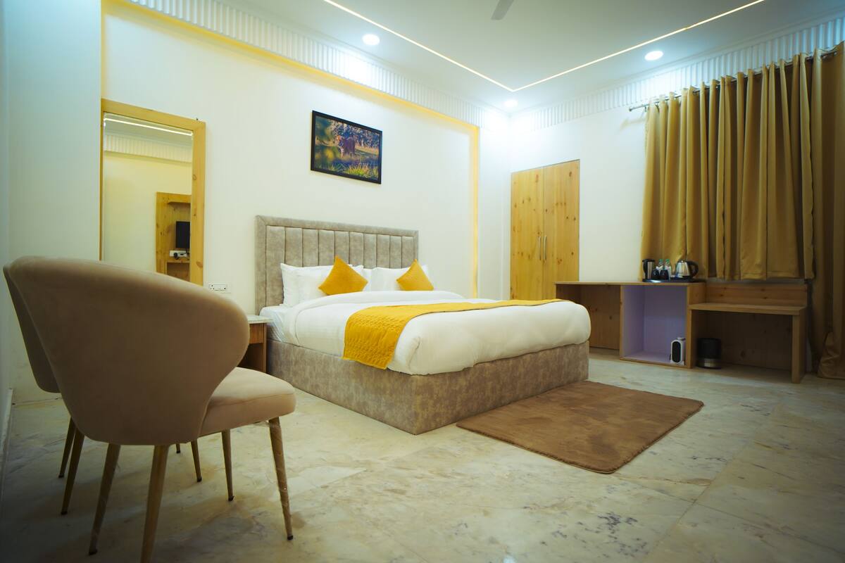 A modern hotel room with a large bed, a wooden wardrobe, a desk, and a chair.