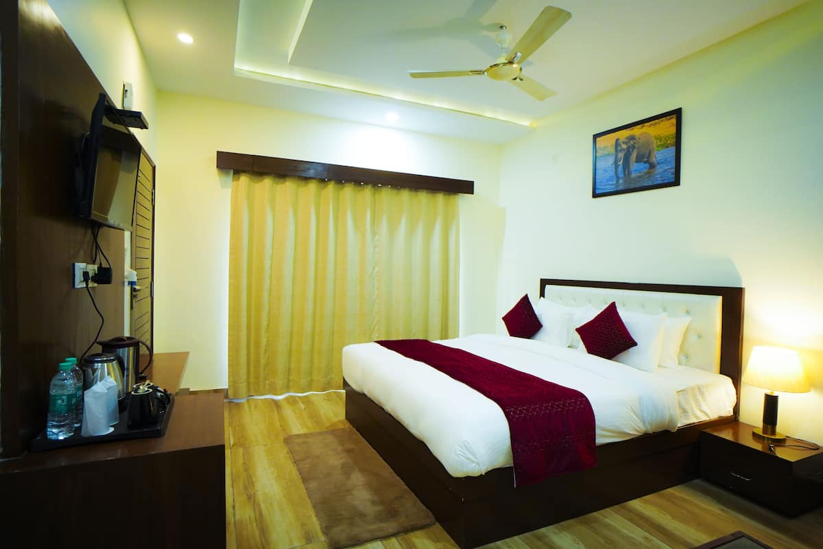 A hotel room with a bed, bedside table, nightstand, ceiling fan, and a painting on the wall.