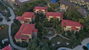 A residential area with multiple two-story houses featuring red-tiled roofs, surrounded by greenery and a swimming pool.