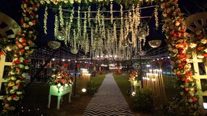 An outdoor venue with a pathway, decorated with hanging lights and floral arrangements.