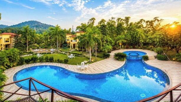 A resort with a large, winding pool surrounded by palm trees and a mountainous backdrop.