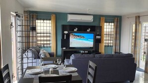 A living room with a TV, sofa, and dining table set up. - Sea Front Villa  (Pool AC Gated 24hrs Security) (St. Catherine Parish Bridgeport P.O)