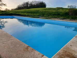 Une piscine rectangulaire à l’eau d’un bleu limpide, entourée d’une terrasse en béton.
