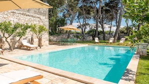 Ein Swimmingpool mit Liegestühlen und einem Tisch, umgeben von Steinmauern und Bäumen.