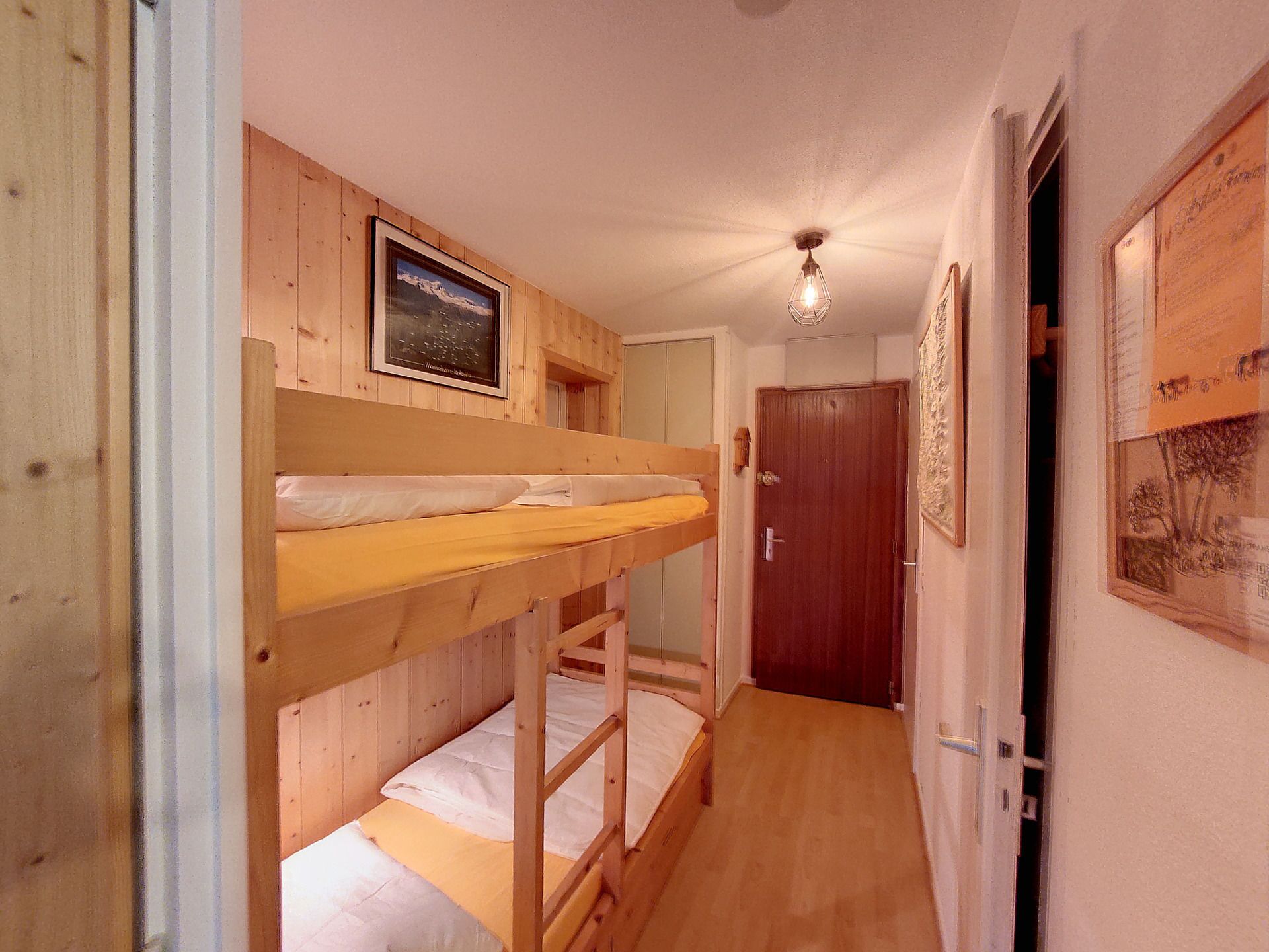 A narrow hallway with bunk beds, wooden walls, a framed picture, and a door at the end.
