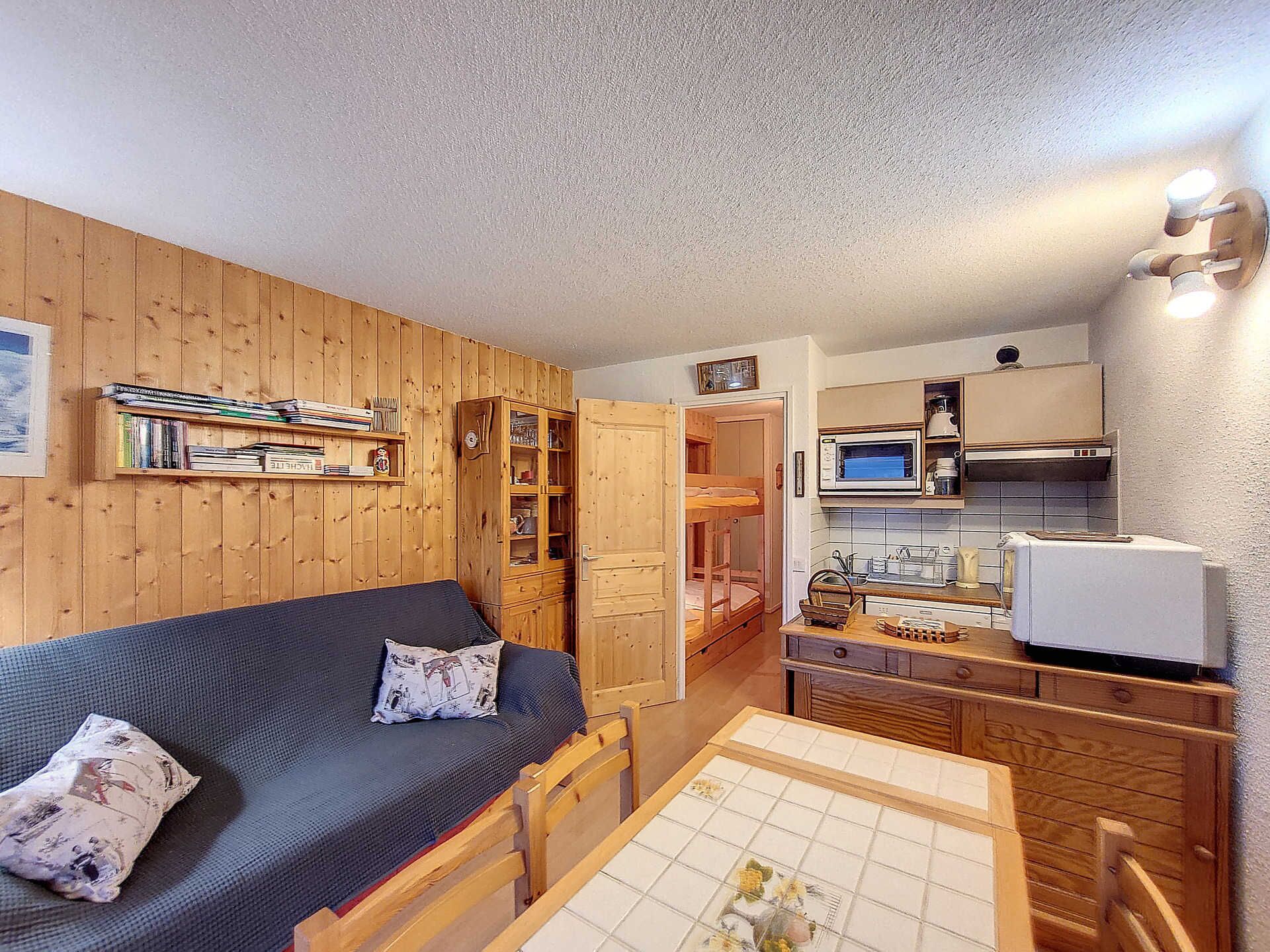 A compact room with a wooden bunk bed, a small kitchenette, and a dining table.