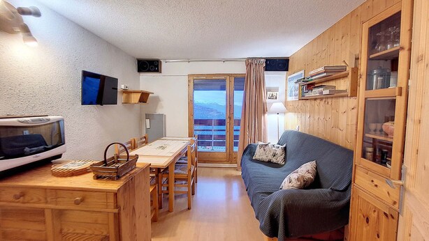 A compact living space with a wooden interior, a dining area with a table and chairs, a sofa, and a television. - Cozy Apartment - Balcony with valley view - 5 minutes from the slopes (Montvalezan)