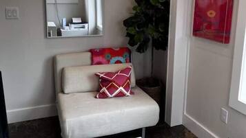 Una habitación pequeña con un sofá blanco, un espejo, una planta en maceta y un cartel rojo en la pared.