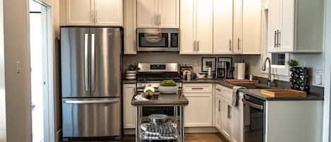A modern kitchen with stainless steel appliances, white cabinetry, and a central island with a microwave and stove.