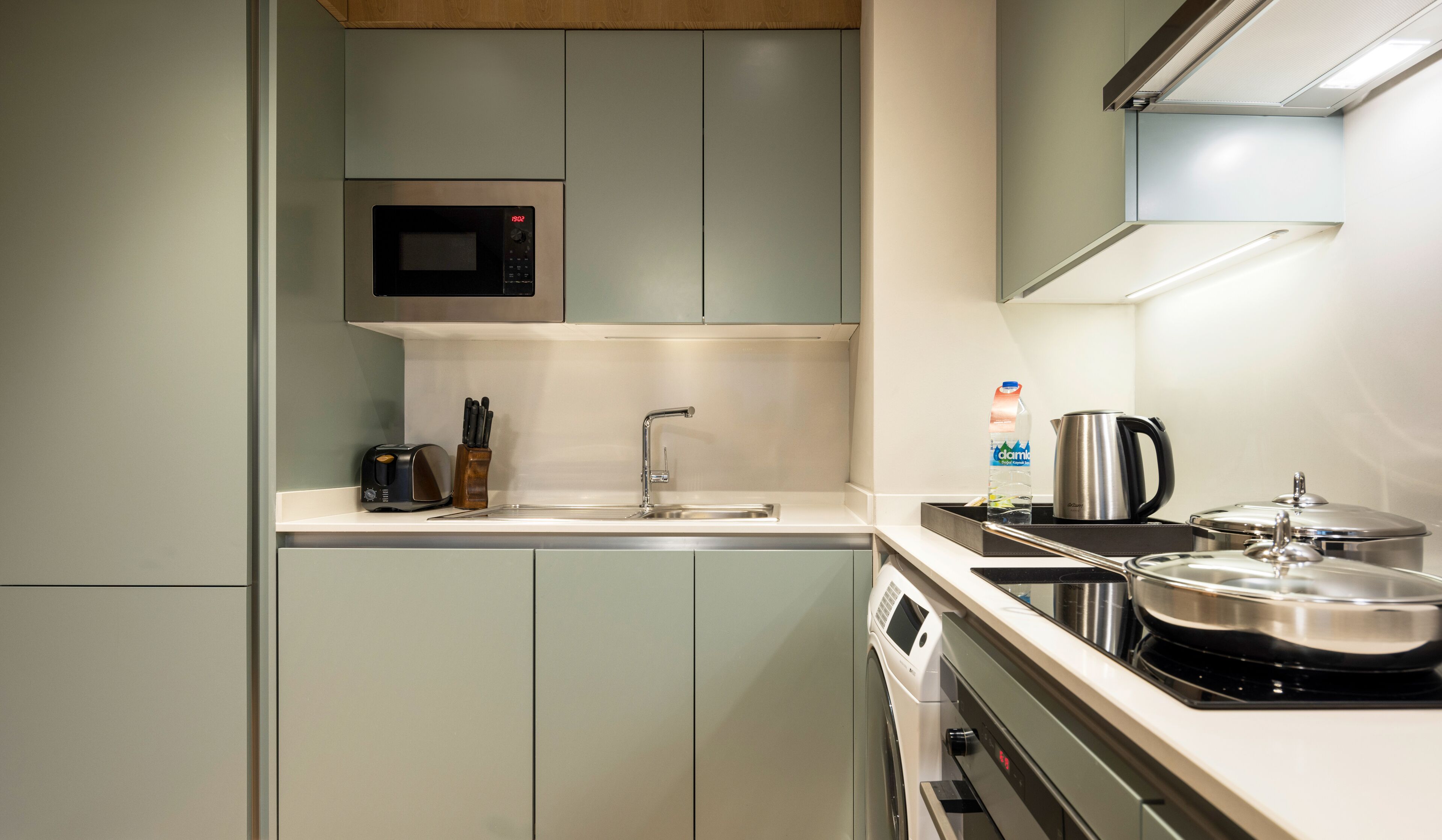 A compact kitchen with a microwave, sink, toaster, and a kettle.