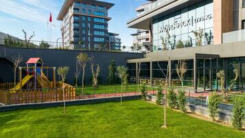 A playground with slides and climbing structures, surrounded by a well-maintained lawn and a building with a large glass facade.