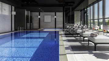 Una piscina interior moderna con superficie de agua azul cristalina, zona de estar contigua con asientos y grandes ventanales que ofrecen luz natural.