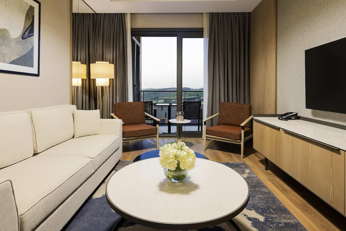 A hotel room with a sofa, two armchairs, a coffee table with flowers, a TV, and a phone on a desk.