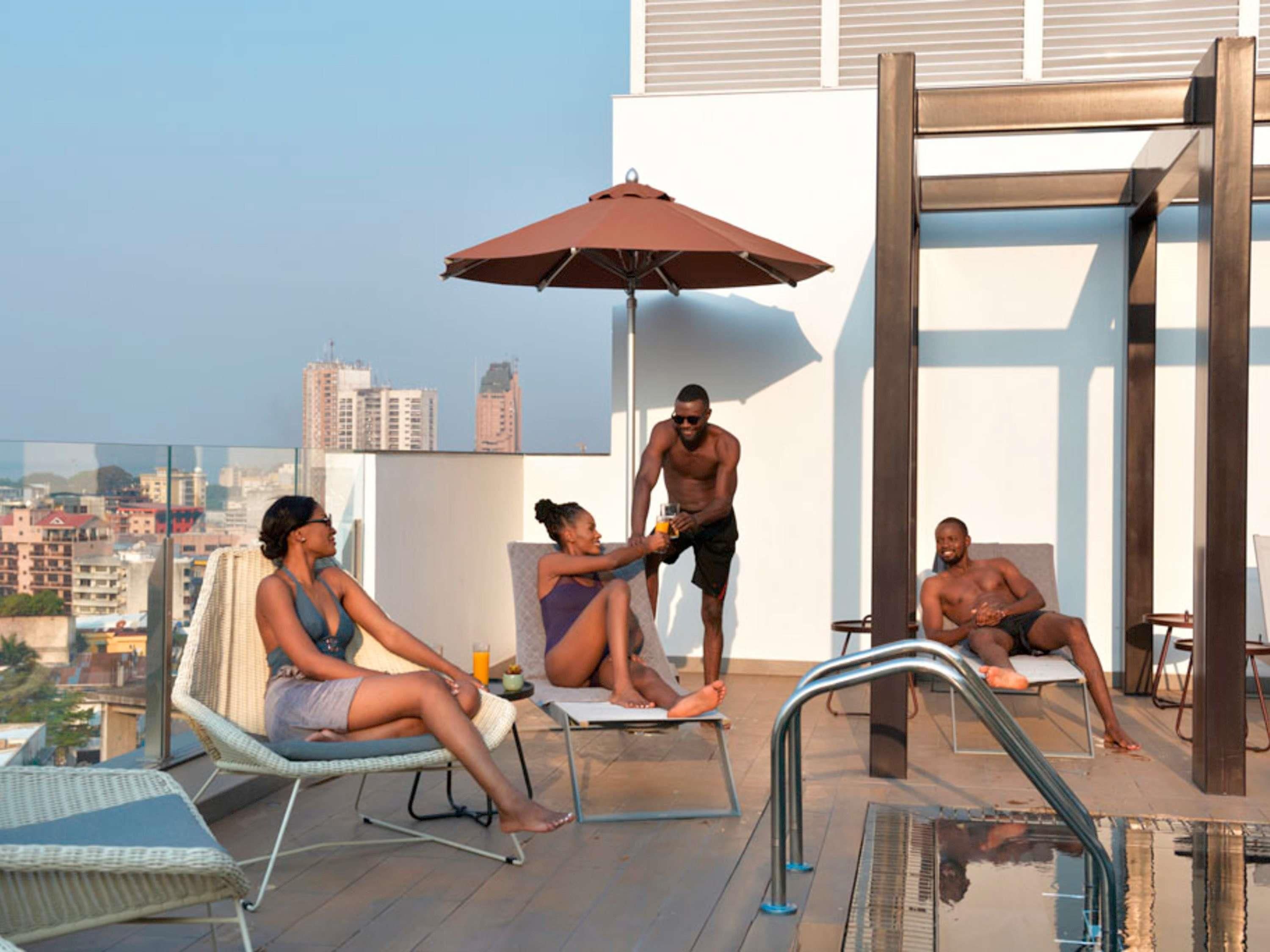 Area piscina sul tetto con poltrone relax, tavolino da biliardo e vista sulla città.
