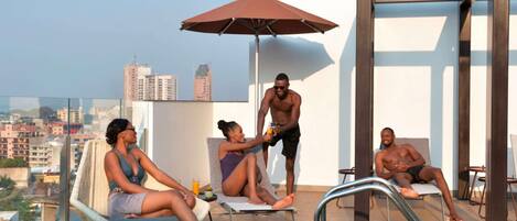 A rooftop pool area with lounge chairs, a pool table, and a view of the cityscape.