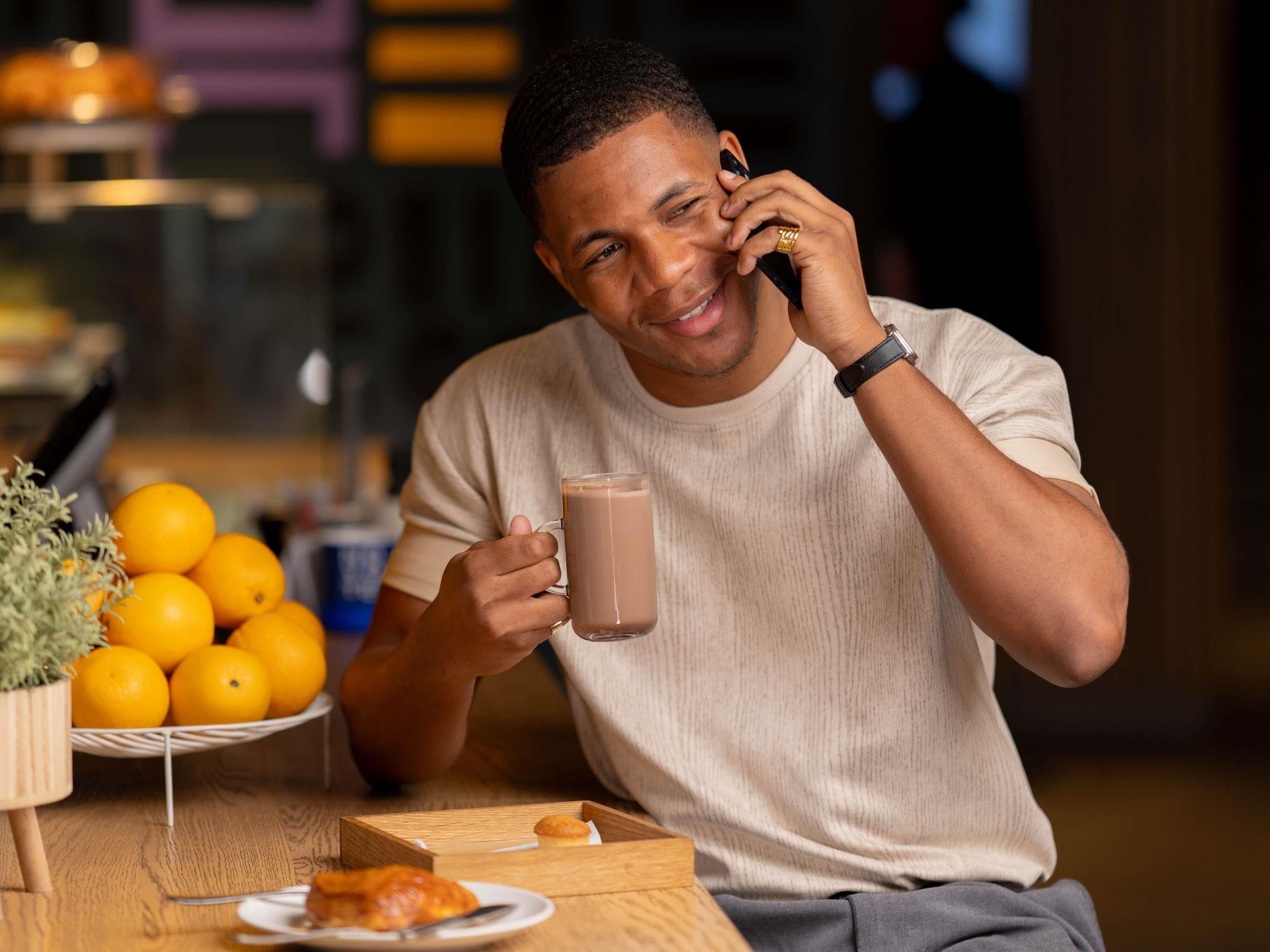 Une personne assise à une table, devant une tasse, des oranges et des pâtisseries.