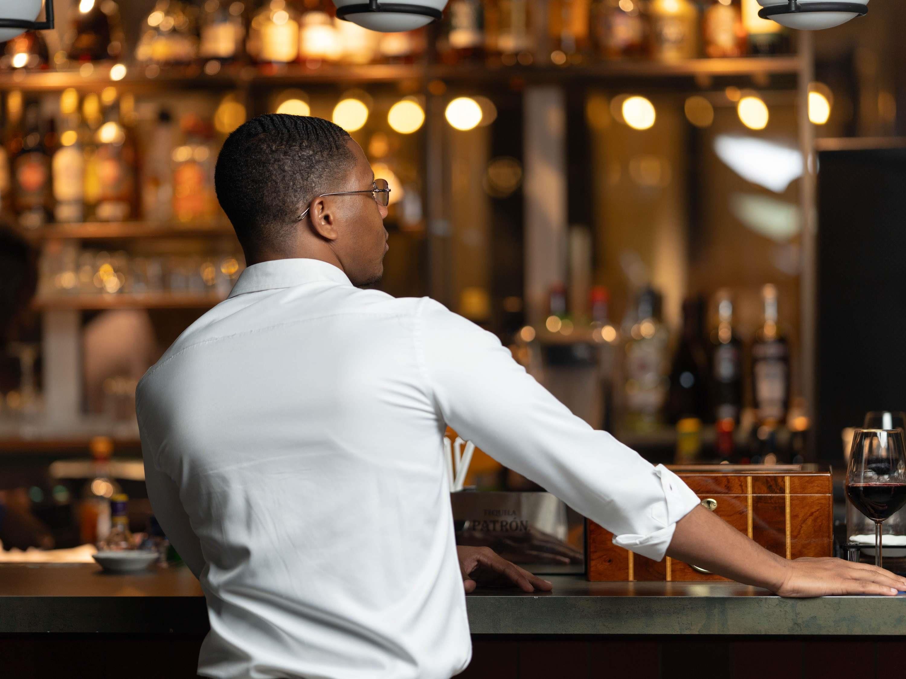 A person standing at a bar counter with a bottle of wine and a glass.