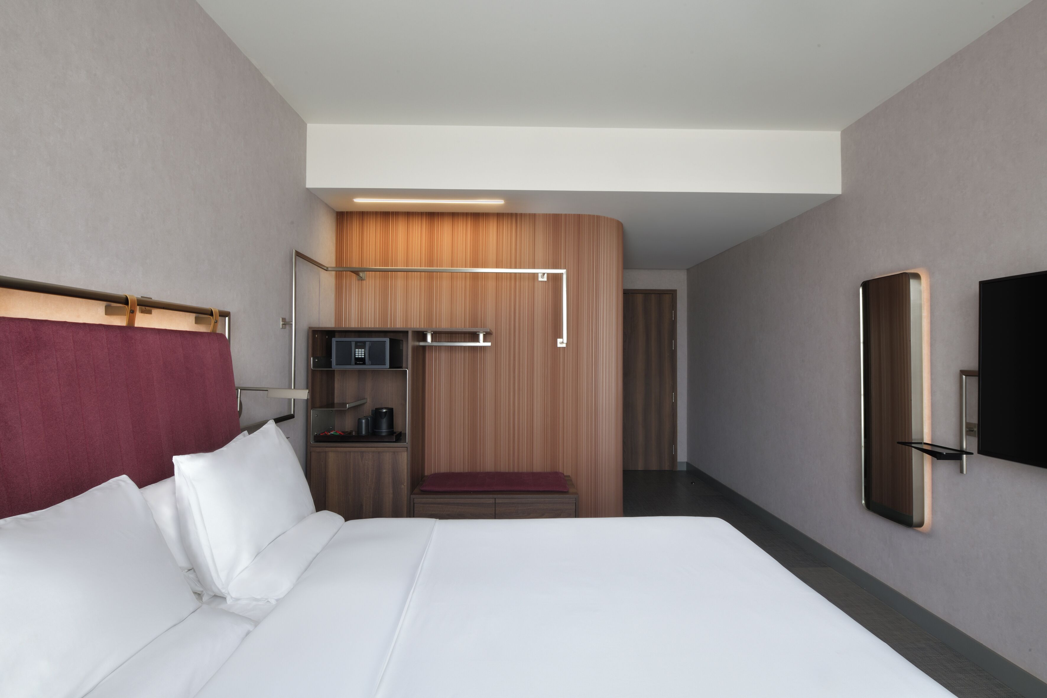 Una habitación de hotel moderna con una cama grande, un panel de pared de madera, una televisión y un televisor de pantalla plana montado en la pared.