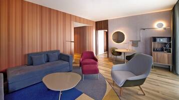 A modern hotel room with a blue sofa, a red chair, a grey armchair, and a round coffee table.