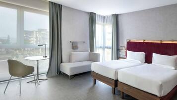 A hotel room with two beds, a sofa, a small table, and a chair.
