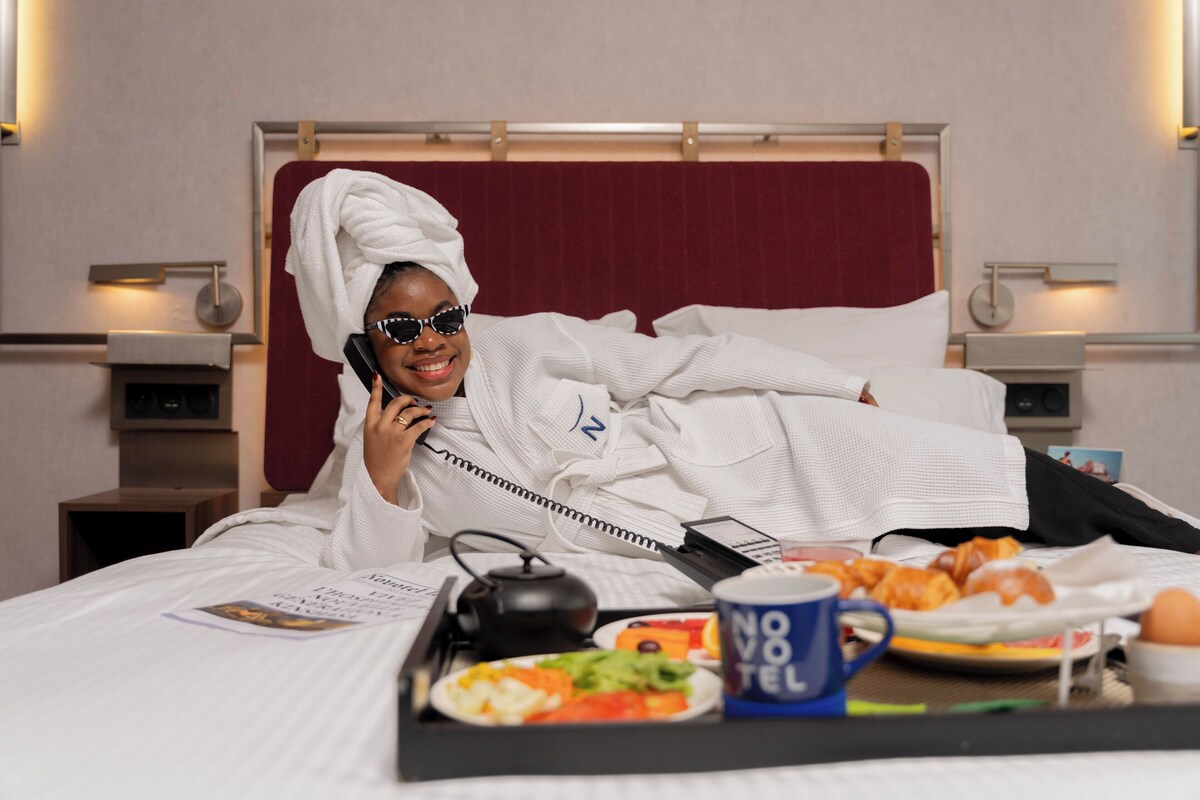 A hotel room with a bed, a bedside table with a lamp, a wall-mounted TV, and a red headboard.