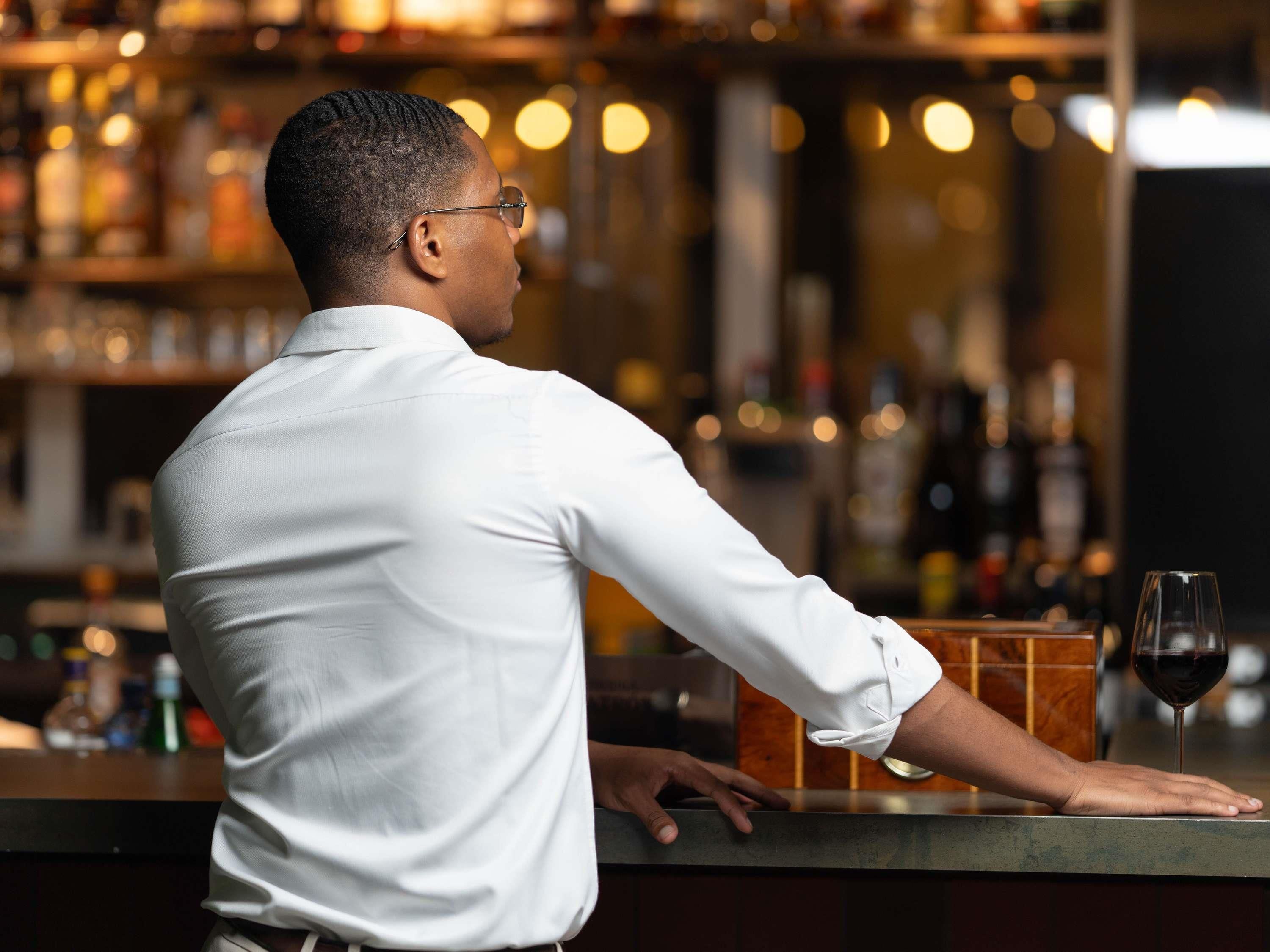 A person in a white shirt leaning on a bar counter with a glass of red wine.