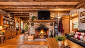 A cozy living room with a stone fireplace, wooden bookshelves, a leather sofa, and a television mounted above the fireplace. - Riverfront Cabin! Farm, Fireplace & Kayaks (DB) (Luray)