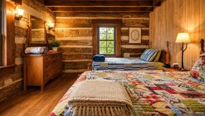 A log cabin bedroom with a bed, dresser, and a window with a view. - Riverfront Cabin! Farm, Fireplace & Kayaks (DB) (Luray)