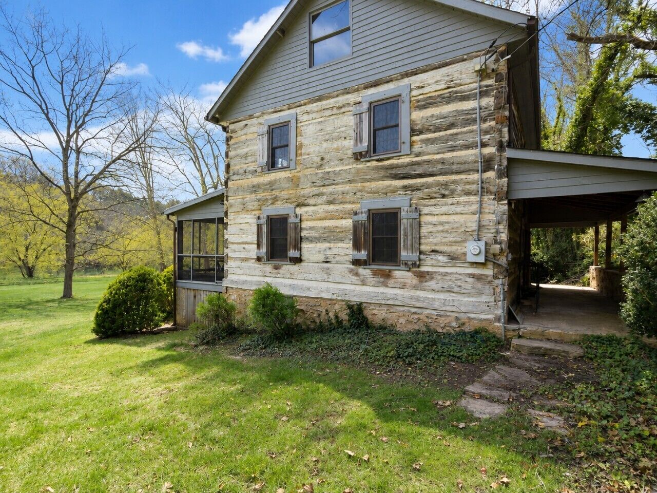 A rustic log cabin with a porch, a covered entryway, and a small front yard with a bush.
