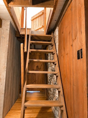 A wooden spiral staircase in a rustic interior with stone walls and wooden floors. - Riverfront Cabin! Mini Highland Cows & Kayaks (DB) (Luray)