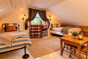 A cozy attic bedroom with two beds, a dining table, and a view of the outdoors.