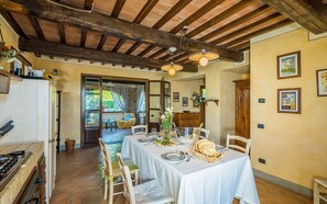 Zona de dinar amb taula preparada per a menjar, bigues de fusta al sostre i vista al jardí a través de la finestra.
