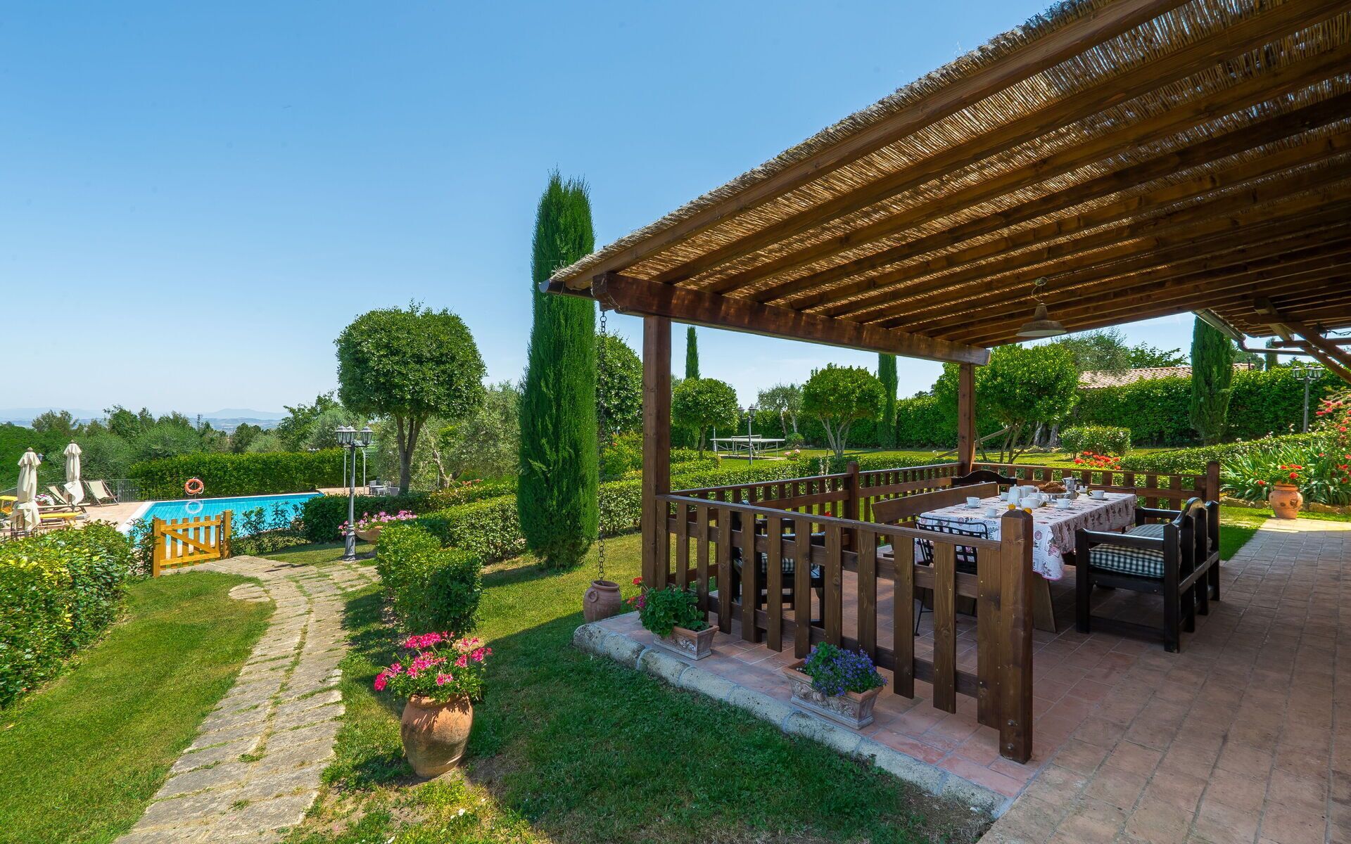 Ein überdachter Essbereich mit Blick auf einen Pool und Garten.