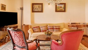 Una sala de estar con un sofá, dos sillones, una mesa de centro, una araña y dos cuadros en la pared.