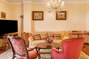 Ein Wohnzimmer mit einer Couch, zwei Sesseln, einem Couchtisch, einer Chandelier und zwei gerahmten Bildern an der Wand.