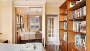 Un dormitorio con una cama, una mesita de noche, una estantería y una puerta que da a otra habitación.