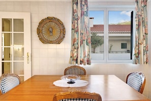 A dining room with a wooden table, checkered chairs, a decorative wall piece, and a window with curtains.