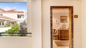 Habitación de hotel con balcón, cómoda de madera, cuadro enmarco y puerta con detalles de mármol.