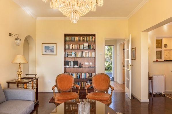 A room with a chandelier, a bookshelf, two chairs, a table, and a lamp.