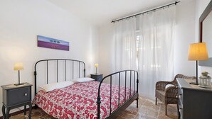 A bedroom with a bed, bedside tables, a chair, a desk, a lamp, and a painting on the wall.