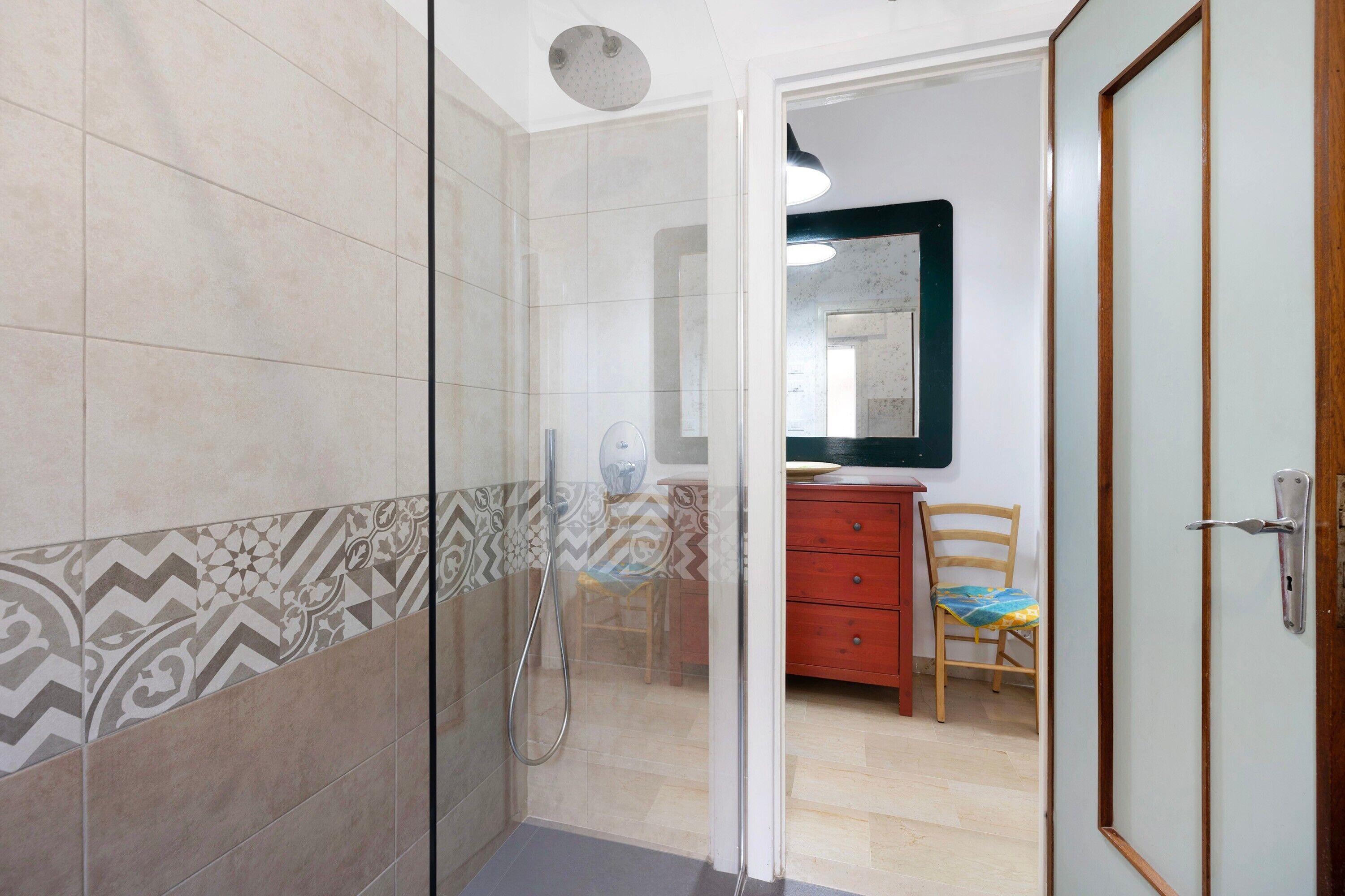 Un bagno con una doccia, uno specchio e una sedia di legno.