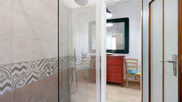 Un bagno con una doccia, uno specchio e una sedia di legno.