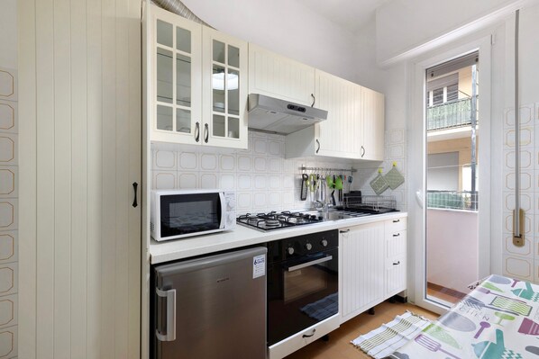 A compact kitchen with white cabinets, a microwave, a gas stove, and a refrigerator.